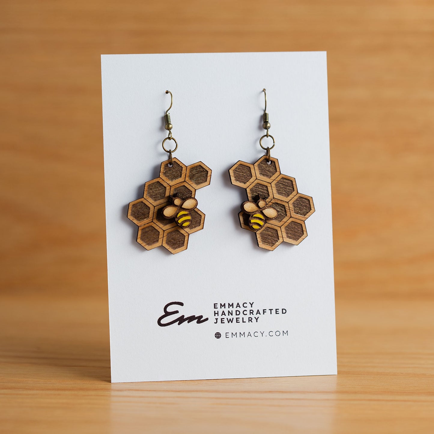 Laser cut wooden dangle earrings in the shape of a honeycomb with a paint bee attached.